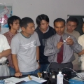 A group of people watching a man demonstrate something at a table with equipment in a classroom or lab.