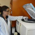 Person in a lab coat and safety goggles using a centrifuge in a laboratory.