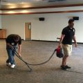 Two men cleaning a large carpeted room with an industrial carpet cleaning machine.