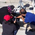 Three individuals examine equipment on a rooftop, one holding a smartphone.