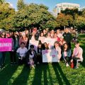 Group of people posing together in a park holding pink breast cancer awareness signs.