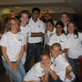 A group of ten people in white t-shirts smiling at the camera indoors.