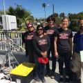 Five people on a rooftop, four in black San Diego State University t-shirts, one in a blue polo, next to an equipment setup and storage box.