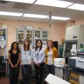 Four women standing in a laboratory with scientific equipment and storage cabinets in the background.