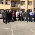 Group of fourteen people standing in front of a yellow and orange building with a PEPFAR sign above them.