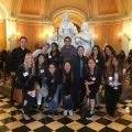 Group of people posing in an ornate indoor space with a marble statue and checkered floor.