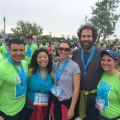 Five people with race bibs and medals posing together at an outdoor event.