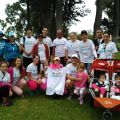 A group of sixteen people gather in a park, most wearing white "PARTNERSHIP" T-shirts, with two children in strollers.