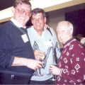 Three men at a social event, smiling and holding drinks.