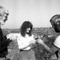 Three people, two men and one woman, laugh and interact outdoors.