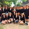 Group of ten people wearing straw conical hats and black shirts, posing together outdoors in a tropical setting.