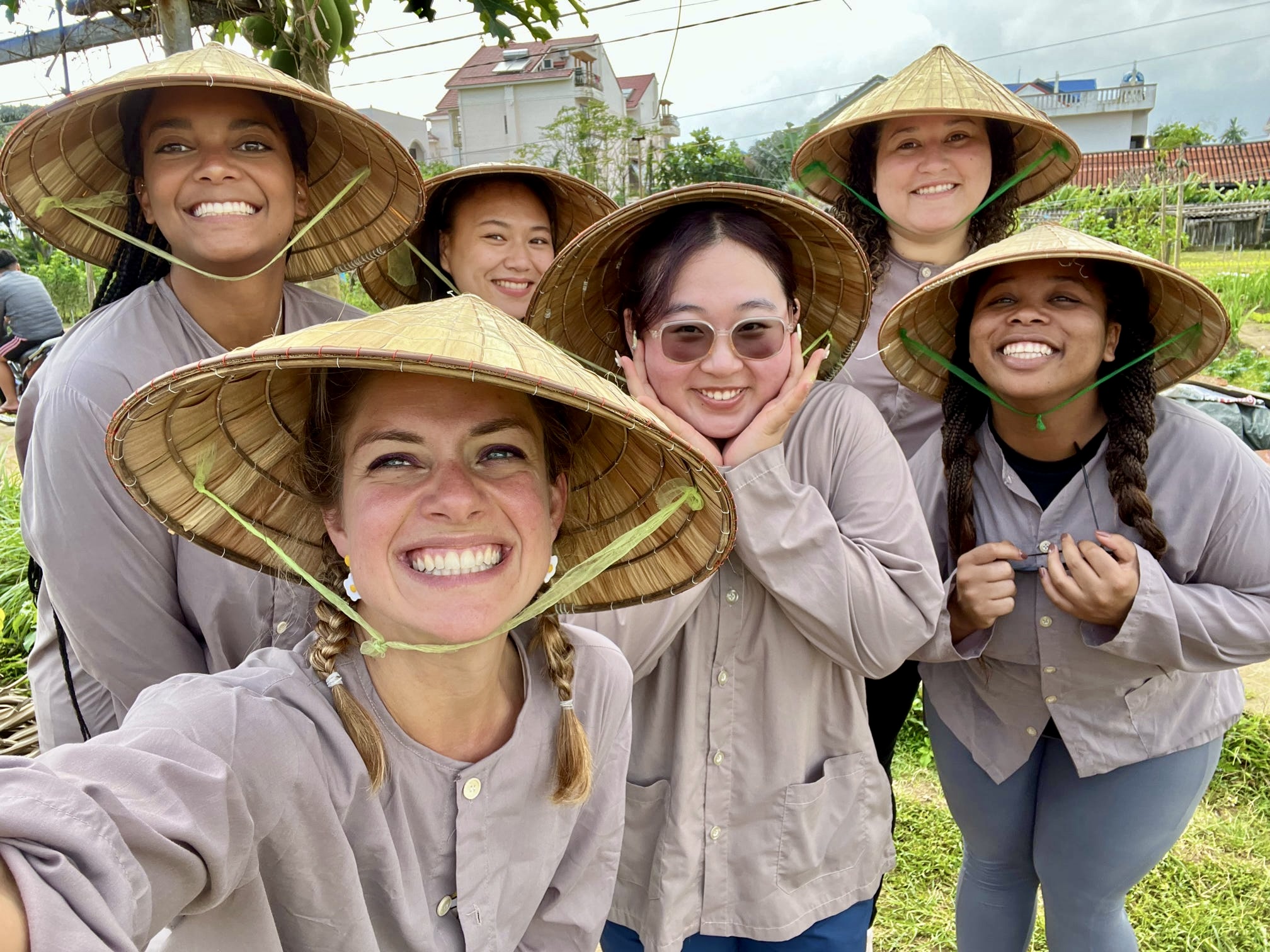 Group of six people wearing conical hats and gray shirts, smiling outdoors.